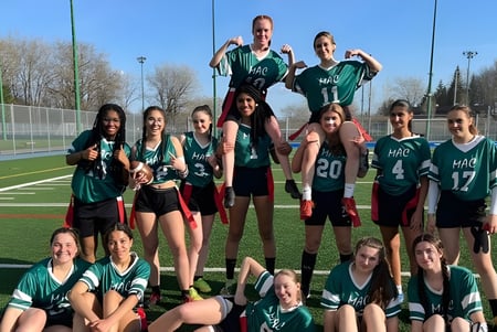 Eine Gruppe junger Sportlerinnen in grünen und schwarzen Trikots posiert auf einem Spielfeld der Macdonald High School.