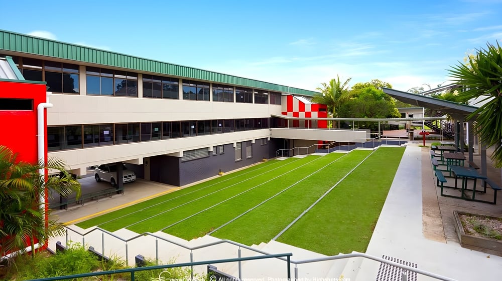 Das moderne mehrstöckige Schulgebäude der MacGregor State High School mit Grünfläche und Palmen im Vordergrund.