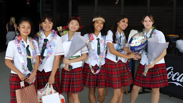Eine Gruppe Schülerinnen steht in traditionellen japanischen Schuluniformen zusammen auf dem Campus der MacGregor State High School.