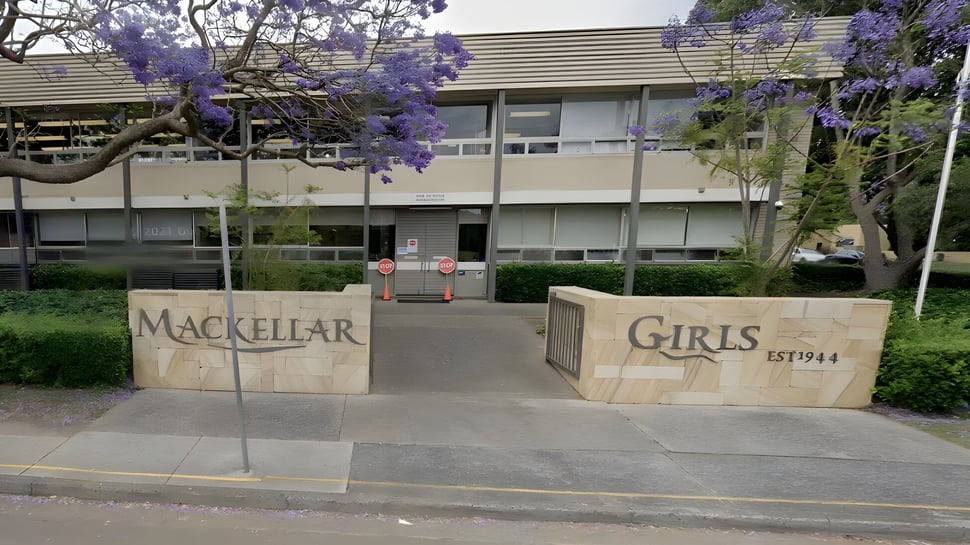 Das Gebäude mit dem Schild Mackellar Girls Campus ist umgeben von Bäumen mit violetten Blüten.