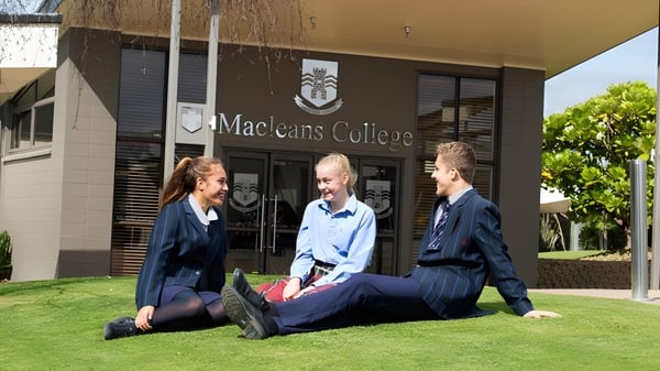 Drei Schülerinnen und Schüler sitzen auf der Wiese vor dem Gebäude des Macleans College.