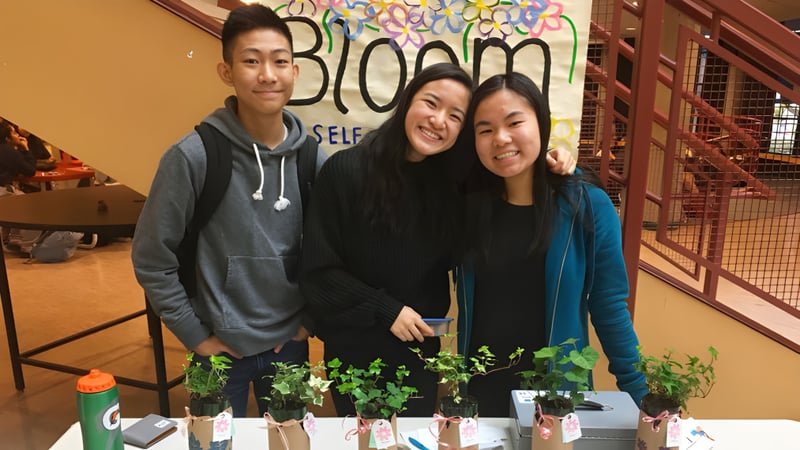 Drei Schülerinnen und Schüler der Magee Secondary School stehen vor einem farbenfrohen Wandbild mit dem Schriftzug Bloom.