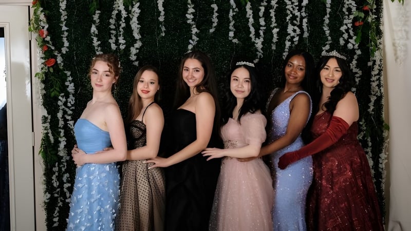 Fünf junge Frauen der Maharishi School posieren gemeinsam vor einem Blumenhintergrund in unterschiedlichen formellen Kleidern.