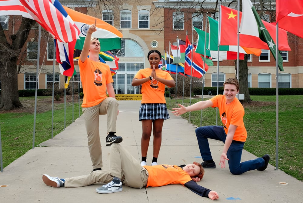 Schüler der Maharishi School stehen in orangefarbenen Shirts vor einem Campusgebäude mit internationalen Flaggen.