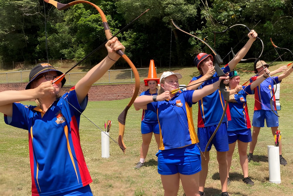 Schüler der Malanda State High School üben im Freien Bogenschießen auf einem mit Grün umgebenen Sportplatz.