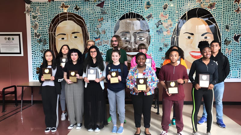 Eine Gruppe von Schülerinnen und Schülern steht vor einem bunten Wandbild auf dem Schulgelände der Mallard Creek High School.
