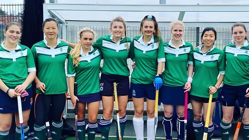 Eine Gruppe von Athletinnen steht vor dem eingezäunten Sportplatz auf dem Campus des Malvern College.