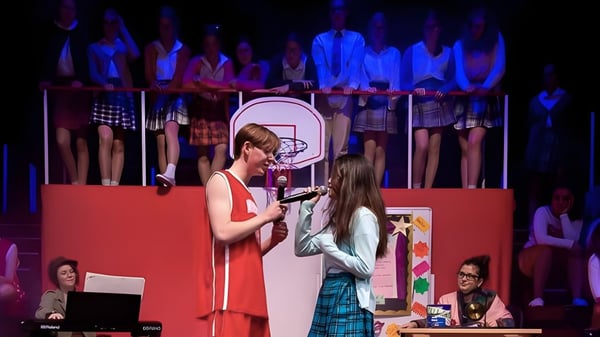 Eine Frau in rotem Kleid und ein Mädchen im karierten Rock stehen bei einer Aufführung auf der Bühne des Malvern College.