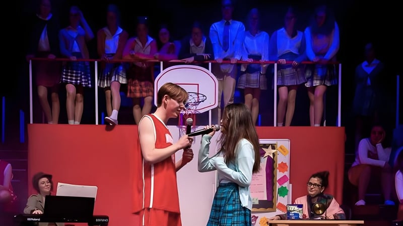 Eine Frau in rotem Kleid und ein Mädchen im karierten Rock stehen bei einer Aufführung auf der Bühne des Malvern College.