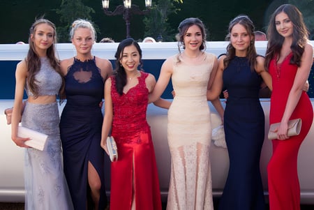 Sechs elegant gekleidete Frauen vom Malvern College posieren vor einer Limousine im Grünen.