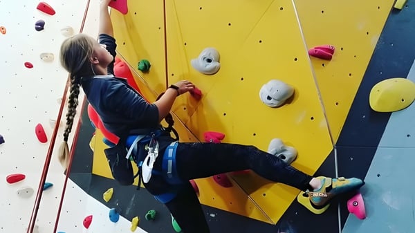 Eine Person mit Kletterausrüstung erklimmt die bunte Kletterwand auf dem Campus des Malvern College.