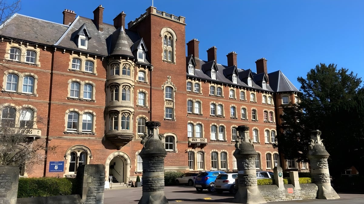 Das historische Hauptgebäude der Malvern St. James Girls' School mit einem Turm und umgeben von Bäumen bei klarem Himmel.