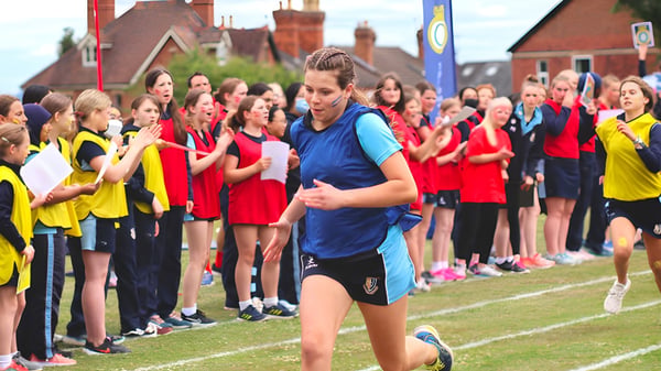 Eine Gruppe junger Athletinnen steht auf dem Sportfeld der Malvern St. James Girls' School mit einer Frau im blauen Trikot im Vordergrund.