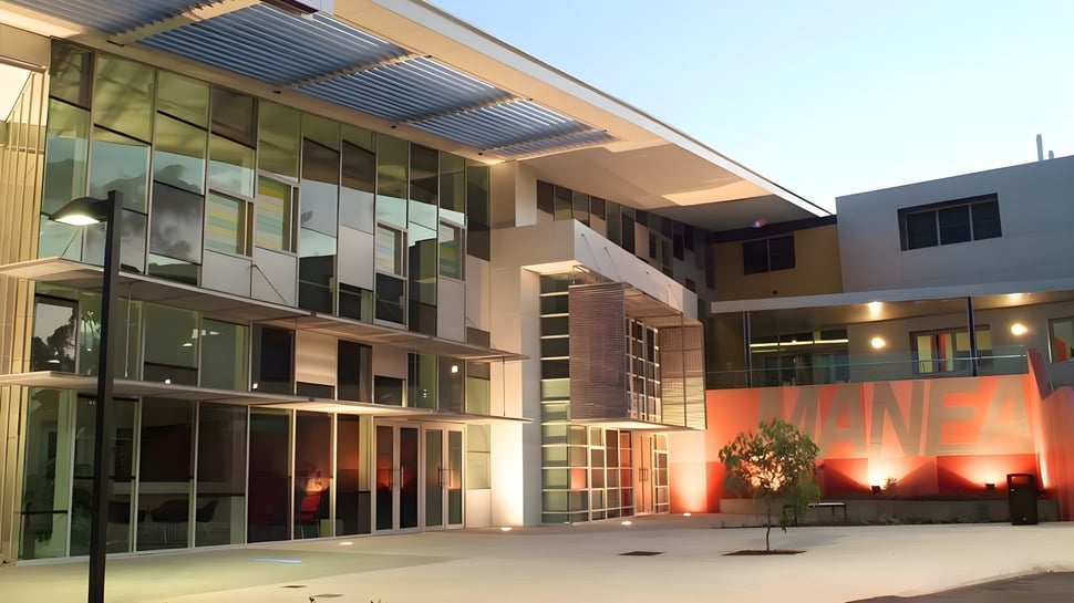 Das moderne Gebäude des Manea Senior College zeigt eine Glasfassade mit überdachtem Eingang und beleuchtetem Außenbereich an einem gepflasterten Hof.