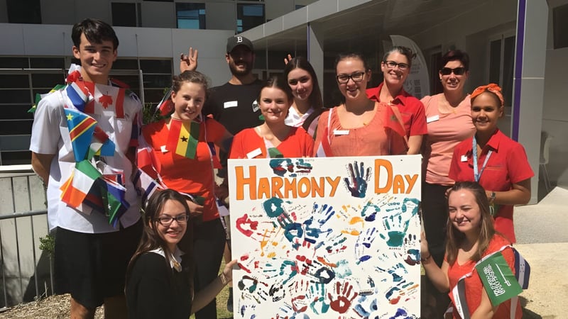 Eine Gruppe von Schülern des Manea Senior College hält ein farbenfrohes Banner mit der Aufschrift Harmony Day vor einem Gebäude.