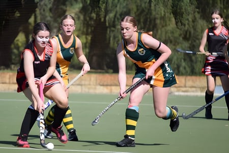 Eine Gruppe von Schülerinnen des Manea Senior College spielt ein Feldhockey-Spiel auf dem grünen Sportplatz.