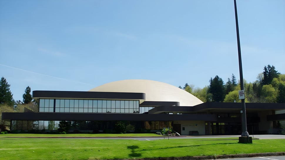 Das kuppelförmige Gebäude mit Glaswänden steht auf dem Campus der Mannahouse Christian Academy umgeben von Rasen und Bäumen.