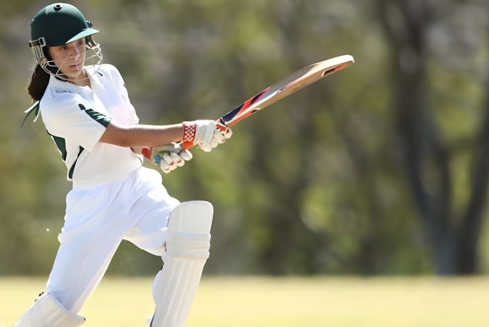 Ein Schüler der Manor House School schlägt den Ball beim Cricket auf dem Sportfeld mit Bäumen im Hintergrund.