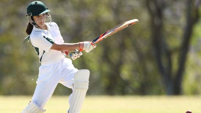 Ein Schüler der Manor House School schlägt beim Cricket auf einem grasbewachsenen Spielfeld mit Bäumen im Hintergrund.