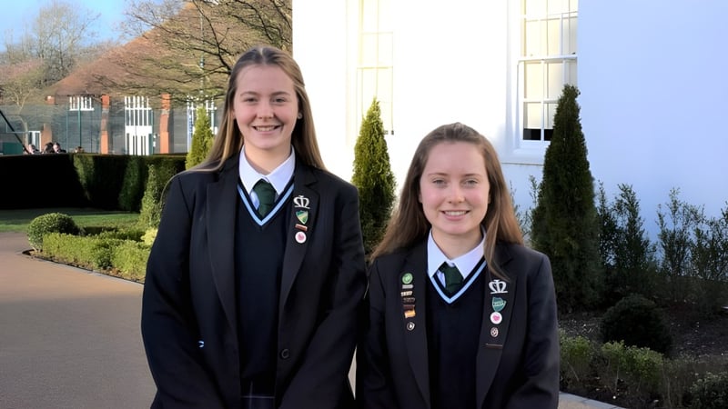 Zwei Schülerinnen der Manor House School stehen draußen zusammen und lächeln vor einem Gebäudekomplex mit Bäumen.