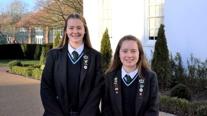 Zwei Schülerinnen in Schuluniformen stehen zusammen und lächeln auf dem Außengelände der Manor House School.