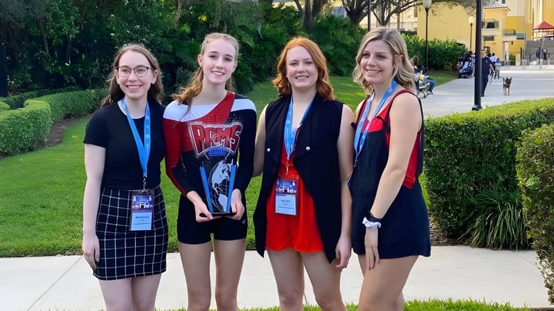 Vier Schülerinnen der Maple Ridge Secondary School stehen zusammen im Freien vor grüner Vegetation und einem gepflasterten Weg.