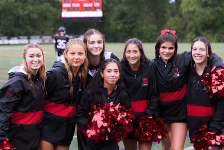Eine Gruppe Cheerleader in schwarzen und roten Uniformen posiert auf dem Sportfeld der Marblehead High School.
