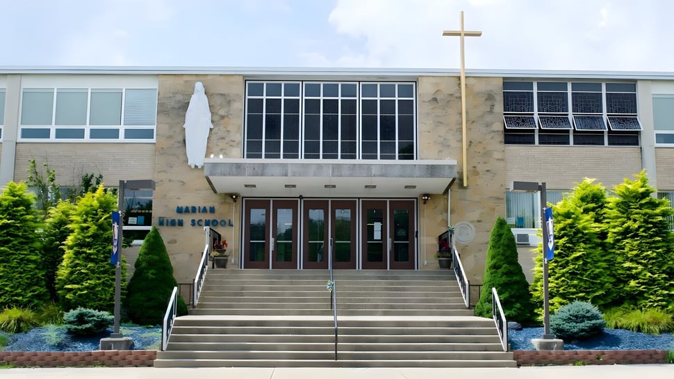 Das große Backsteingebäude der Marian Catholic High School mit einem Kreuz auf dem Dach ist von Grünflächen umgeben.