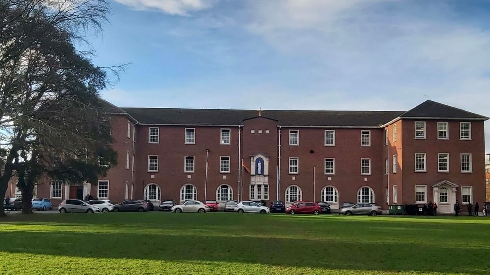 Das große Backsteingebäude des Marian College mit einer Rasenfläche und parkenden Autos davor.