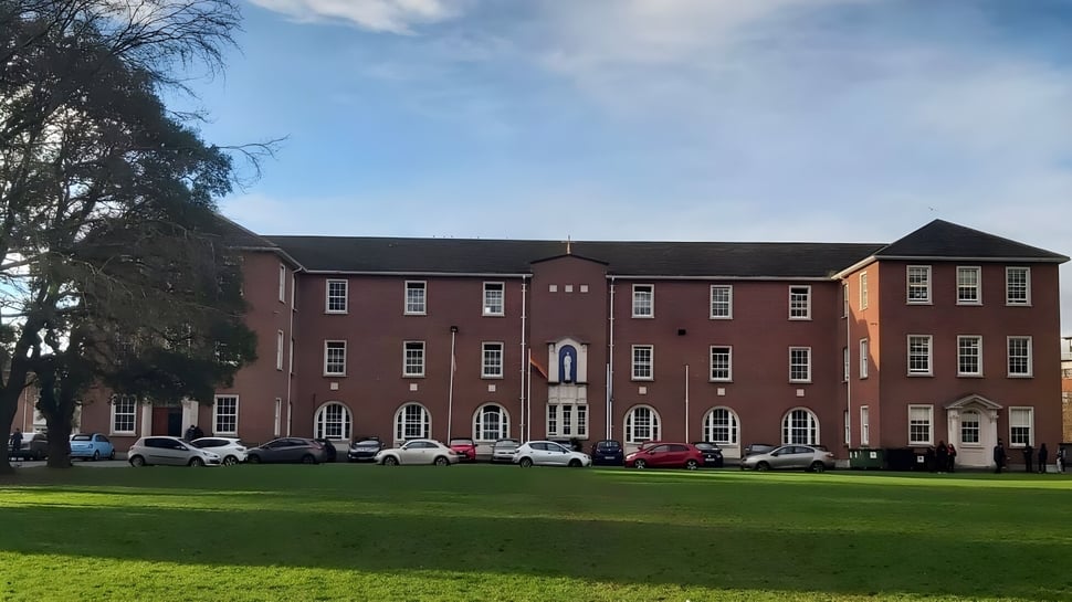 Das mehrstöckige Backsteingebäude mit Bögen auf dem Campus des Marian College vor bewölktem Himmel.