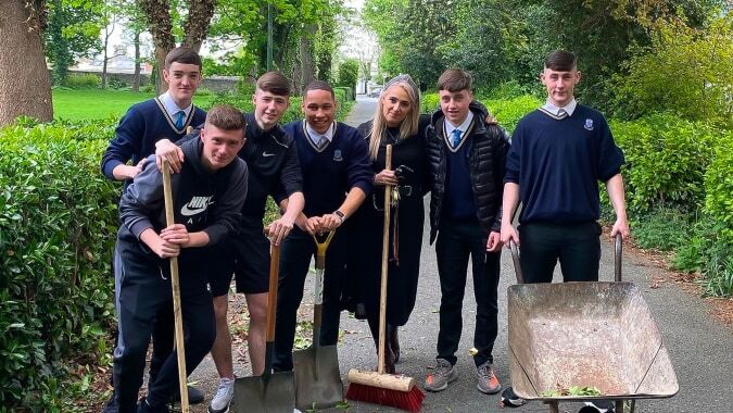 Eine Gruppe von Schülerinnen und Schülern in Schuluniformen steht auf einem Weg mit viel Grün auf dem Gelände des Marian College.
