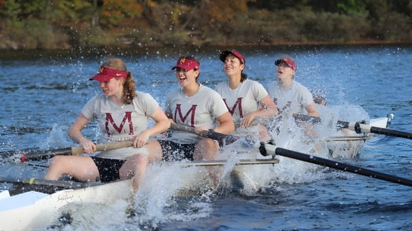 Vier Schülerinnen und Schüler der Marianapolis Preparatory School rudern auf einem See umgeben von herbstlicher Vegetation.