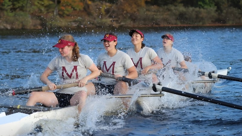 Vier Schülerinnen und Schüler der Marianapolis Preparatory School rudern auf einem See umgeben von herbstlicher Vegetation.