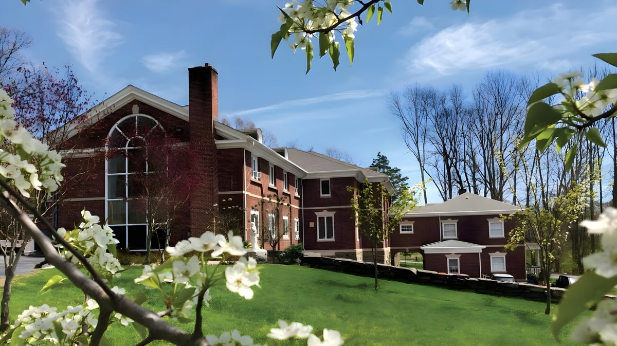 Das Backsteingebäude mit Turm der Marianapolis Preparatory School steht eingebettet in eine grüne Landschaft mit blühenden Bäumen.