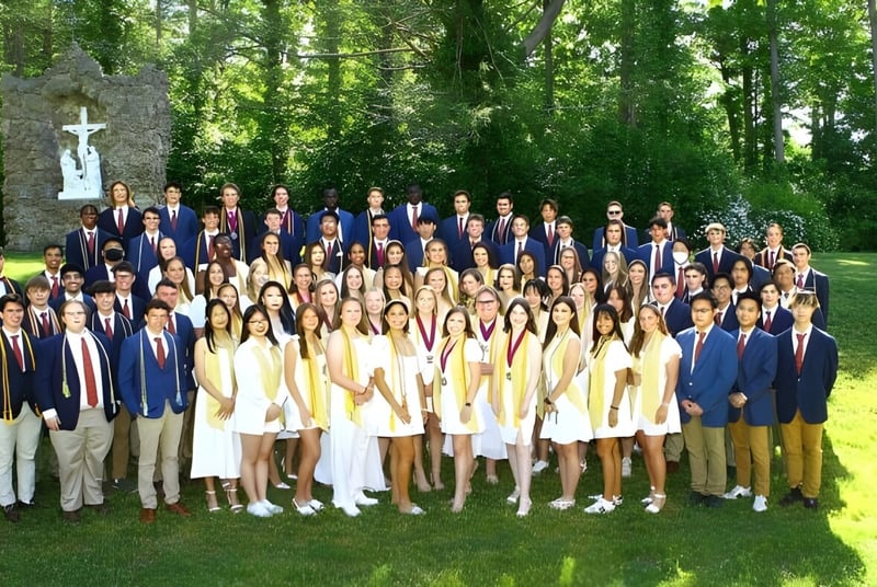 Eine Gruppe Schülerinnen und Schüler der Marianapolis Preparatory School steht in formeller Kleidung vor einem kreuzförmigen Denkmal im Freien.