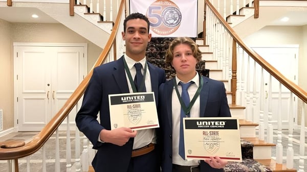 Zwei Schüler der Marianapolis Preparatory School stehen im Treppenhaus und halten Zertifikate der Organisation United.
