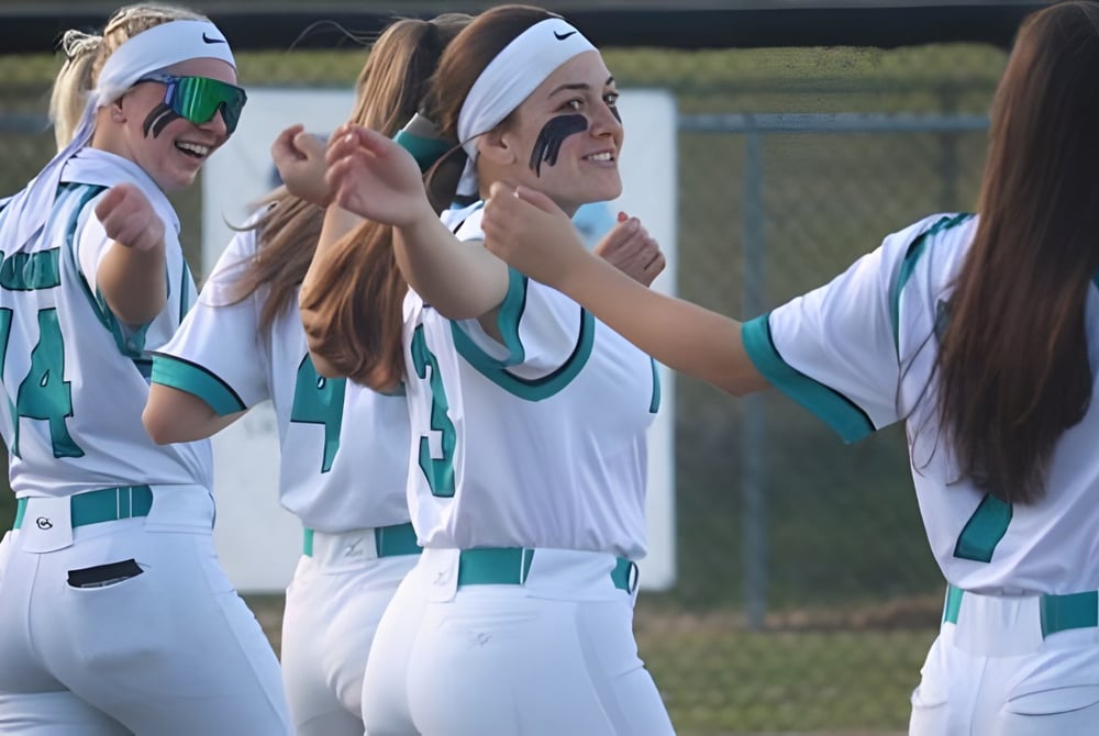 Eine Gruppe junger Athletinnen in weißen und grünen Uniformen steht auf einem Sportfeld und feiert gemeinsam auf dem Campus der Marion County Public Schools.