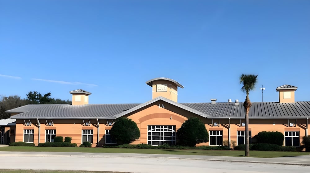 Das Backsteingebäude mit Metalldach und Schornsteinen der Marion County Public Schools ist von Bäumen und Grünflächen umgeben.