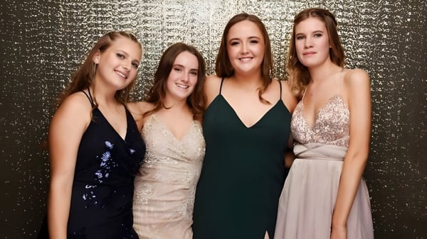 Vier Schülerinnen in festlicher Kleidung posieren vor einem goldenen Hintergrund auf dem Campus des Marist College.