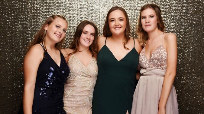 Vier junge Frauen in formeller Kleidung posieren gemeinsam vor goldenem Hintergrund am Marist College.