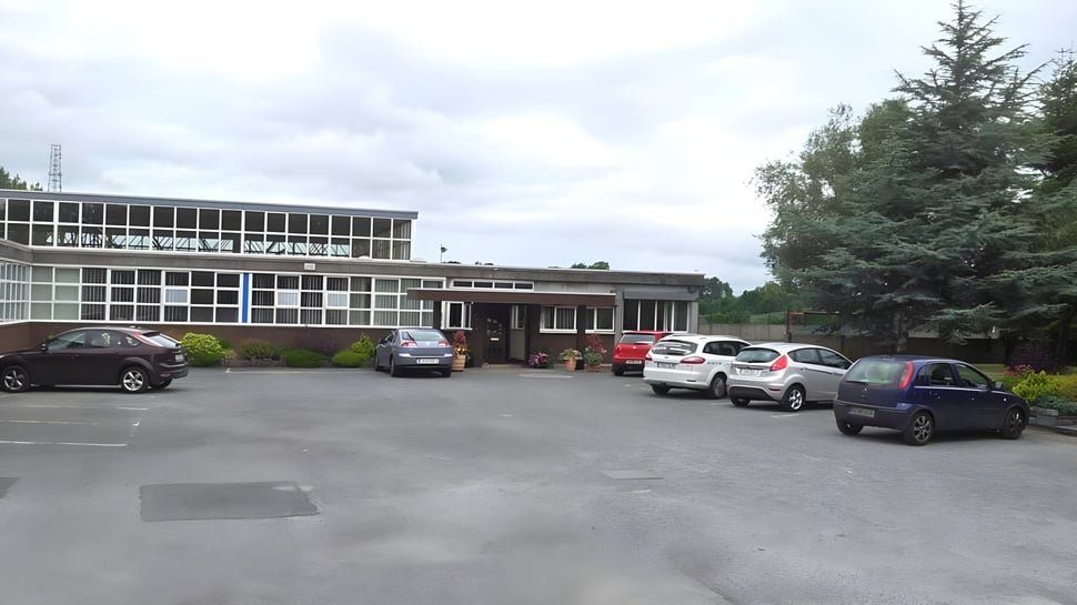 Mehrstöckiges Gebäude des Marist College mit Parkplatz und Bäumen bei bewölktem Himmel.