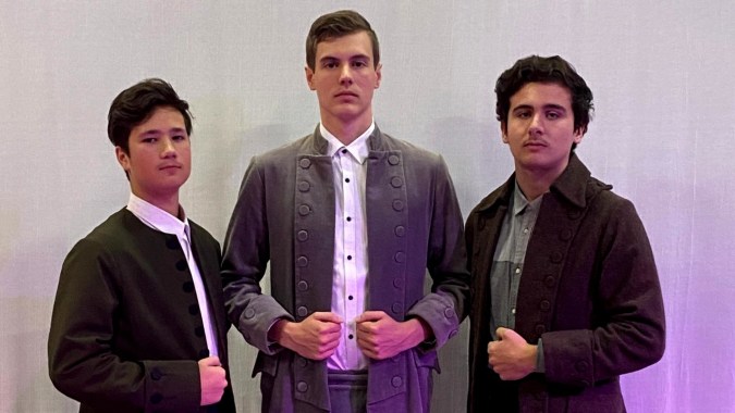 Drei Schüler in formeller Kleidung stehen zusammen vor einem schlichten Hintergrund am Marist College.