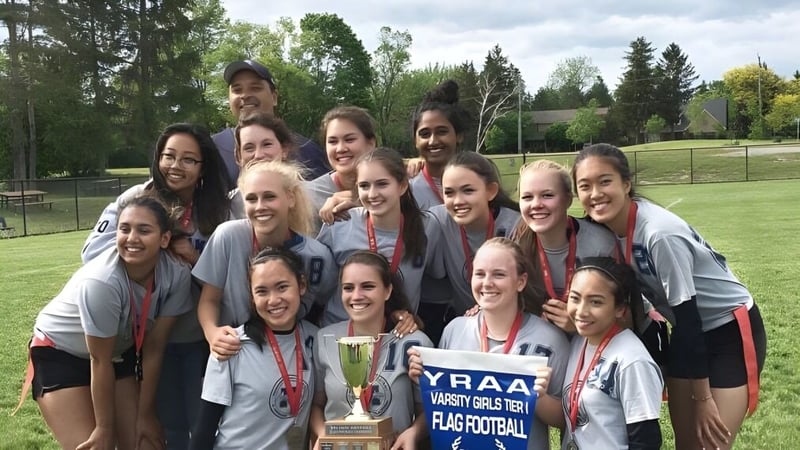 Eine Gruppe junger Sportlerinnen der Markham District High School feiert auf einem Spielfeld mit einem Pokal.