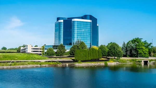 Das moderne Glas- und Stahlgebäude der Markham District High School steht hoch vor klarem Himmel und umgeben von Grünflächen und Wasser.