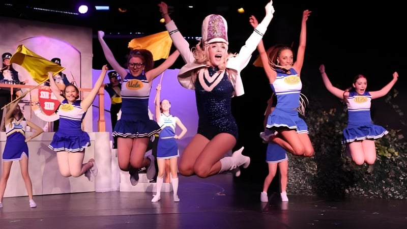 Eine Gruppe Schülerinnen des Marlborough College führt in bunten Kostümen auf der Bühne vor einem beleuchteten Hintergrund auf.