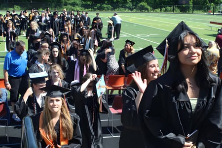 Absolventen des Marlborough College stehen in schwarzer Robe und Barett auf einem Feld und posieren teils winkend.