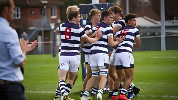 Eine Gruppe junger Athleten in gestreiften Trikots steht auf dem Sportfeld des Marlborough College vor einem Gebäude.