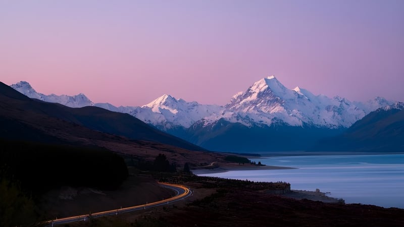 Eine gewundene Straße führt durch eine ruhige Landschaft mit schneebedeckten Bergen im Hintergrund des Marlborough Girls Campus.