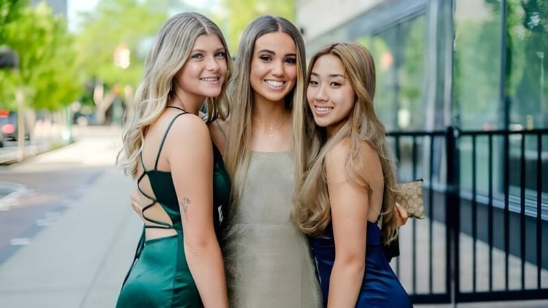 Drei Schülerinnen der Marlborough Girls stehen im Freien zusammen und lächeln vor einem Geländer mit Grün im Hintergrund.