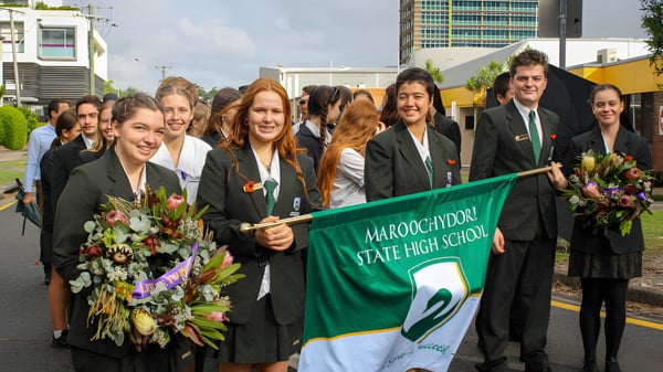 Eine Gruppe von Schülern der Maroochydore State High School trägt Abschlussroben und hält ein Banner vor Hochhäusern.